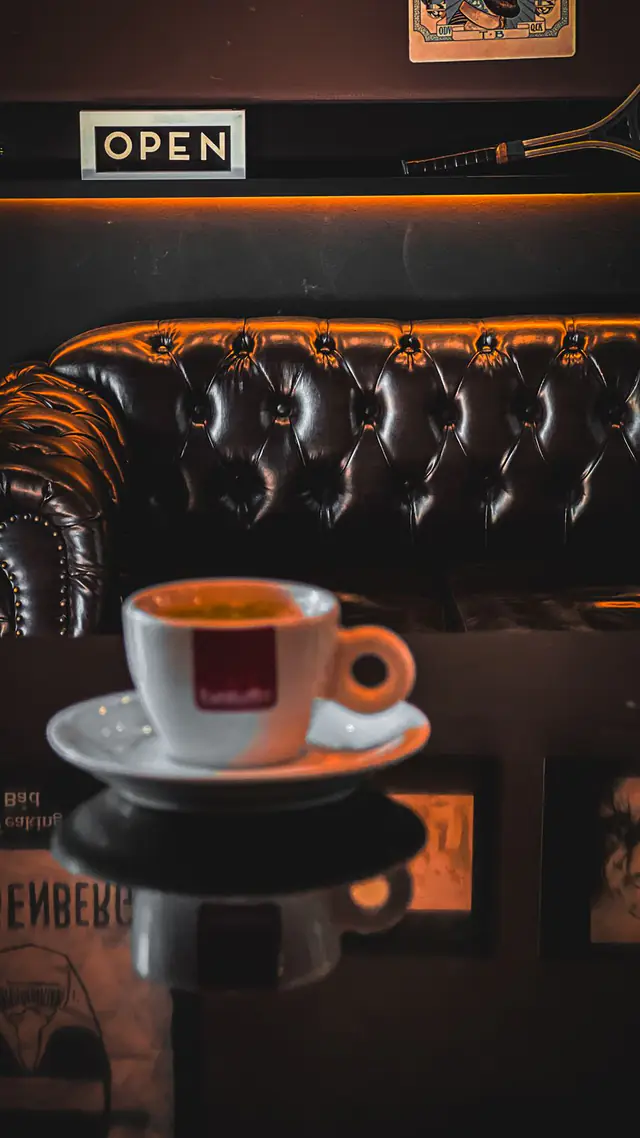 Café expresso servido no lounge, com sofá Chesterfield ao fundo